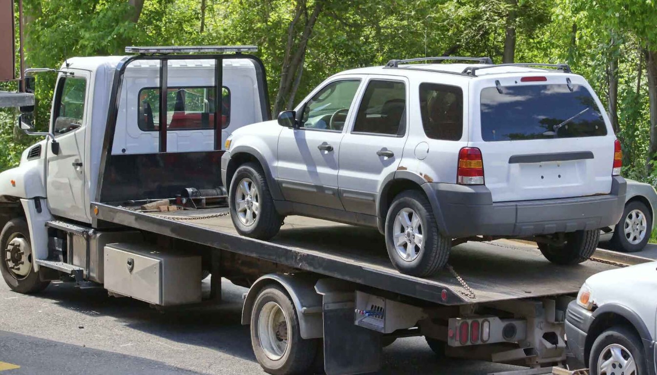 SUV being transported long distance on white flatbed tow truck